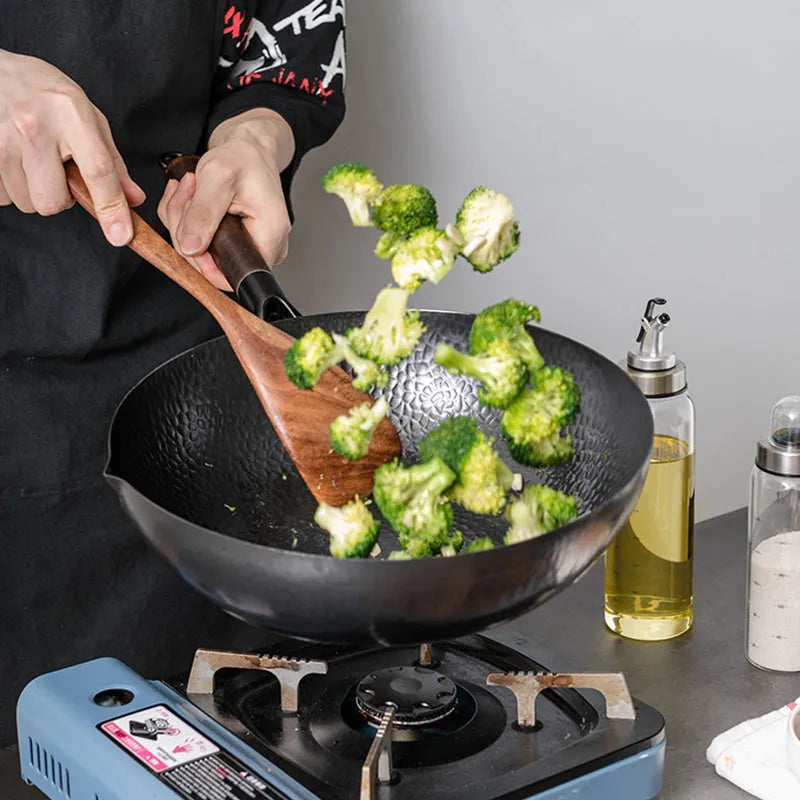 Black traditional cast iron wok pan with wooden handle and glass lid on induction hob
