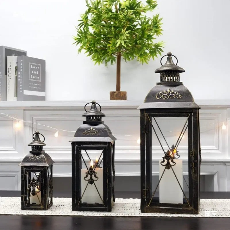 Black and white wrought iron floor-standing storm lantern with clear tempered glass panels on a garden patio.