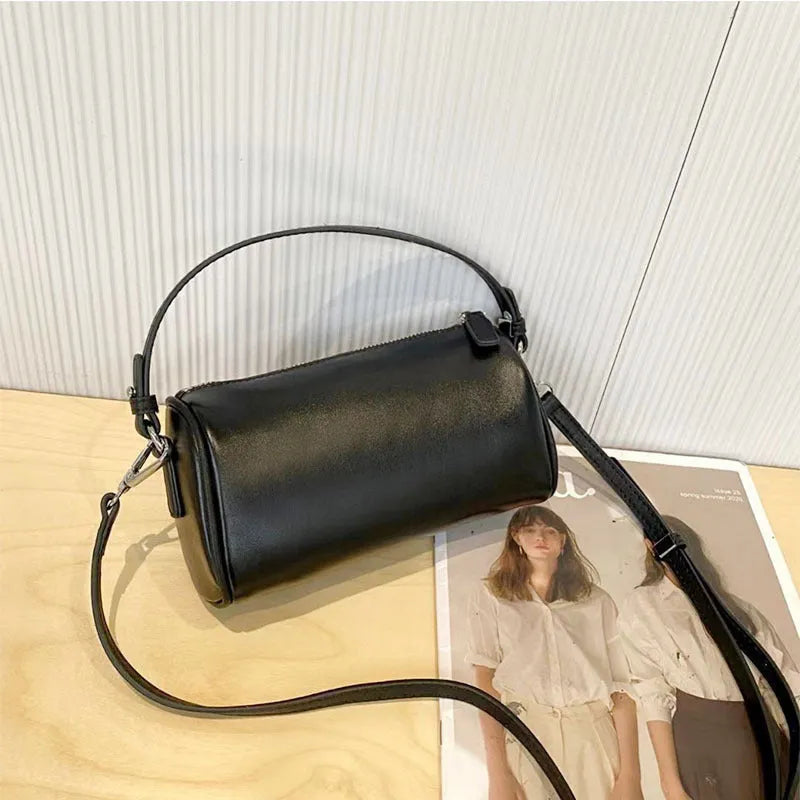 Men's cylindrical leather crossbody phone bag in black, shown with visible stitching and shoulder strap