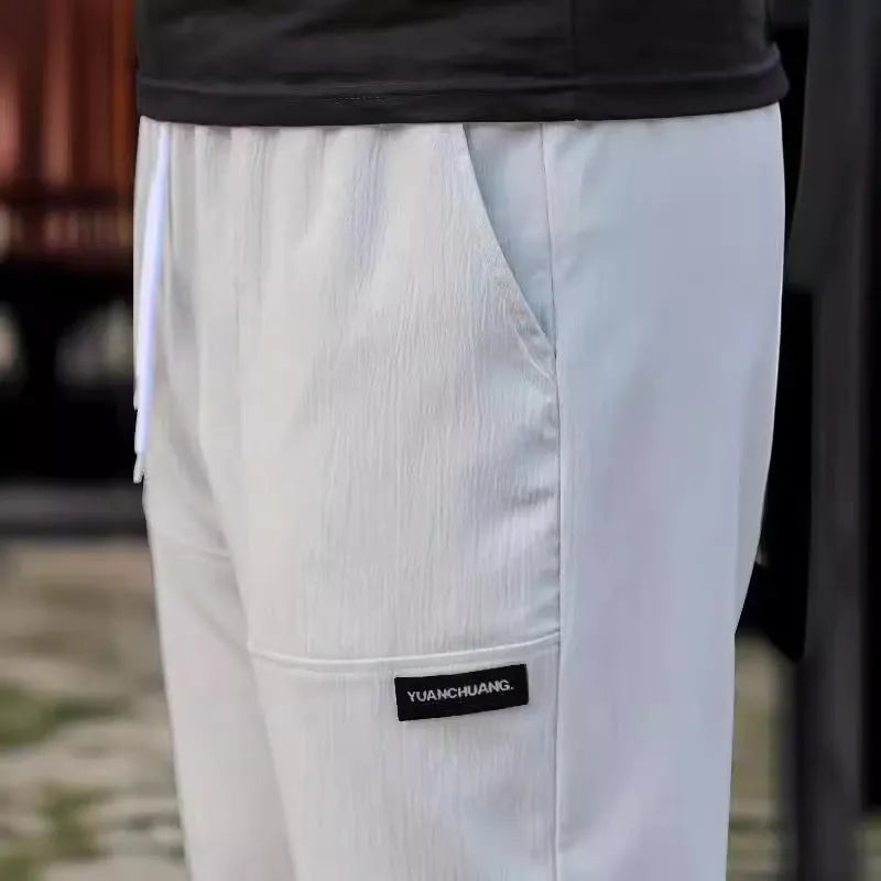 Men's polyester trousers in light grey colour, shown folded, for spring and autumn wear.