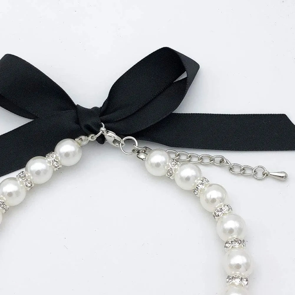 Small dog wearing an adjustable blue pearl and rhinestone necklace with a ribbon bow on a soft ribbon.