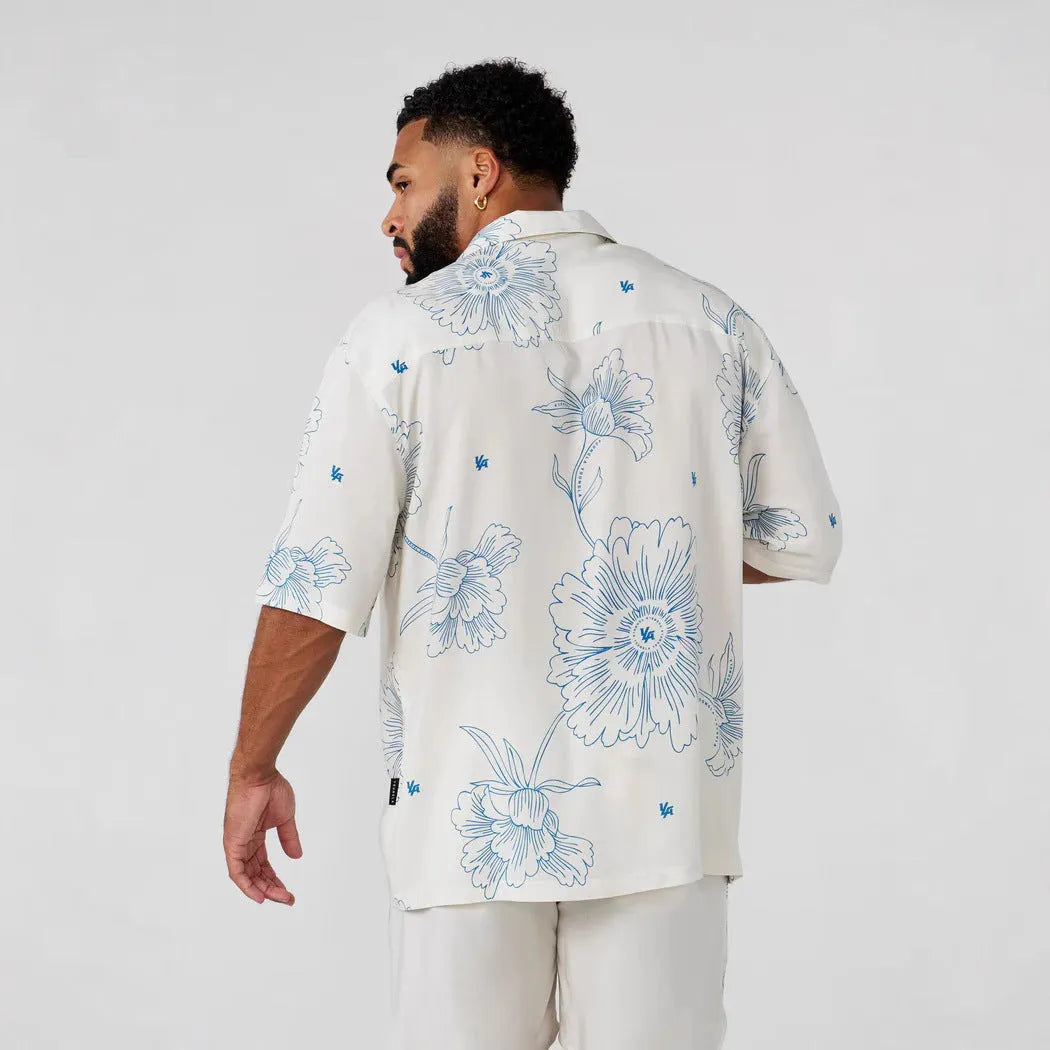 Man wearing a loose grey short-sleeve top with a floral print pattern.