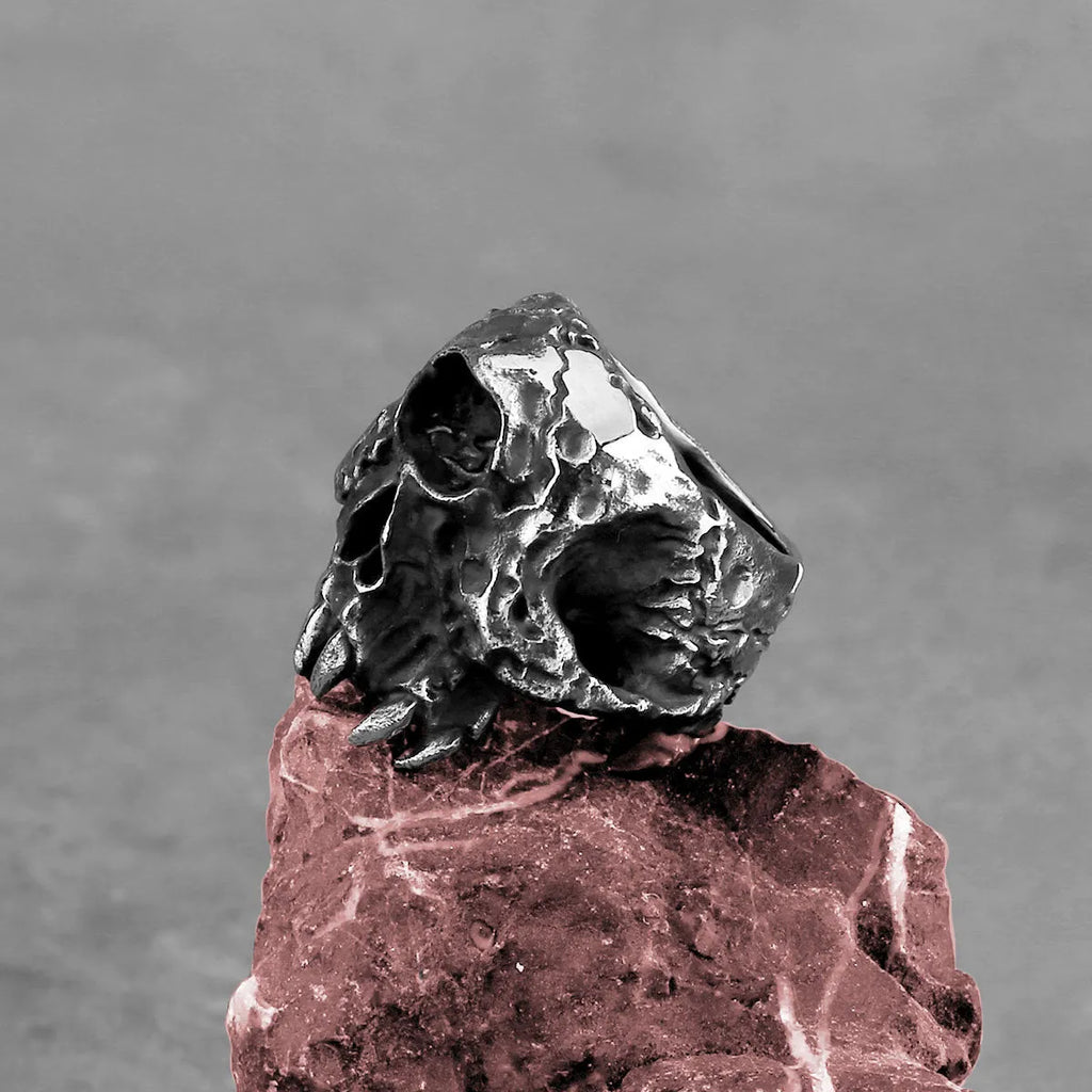 Close-up of a silver-toned alloy ring featuring a detailed one-eyed skull design on a black background.