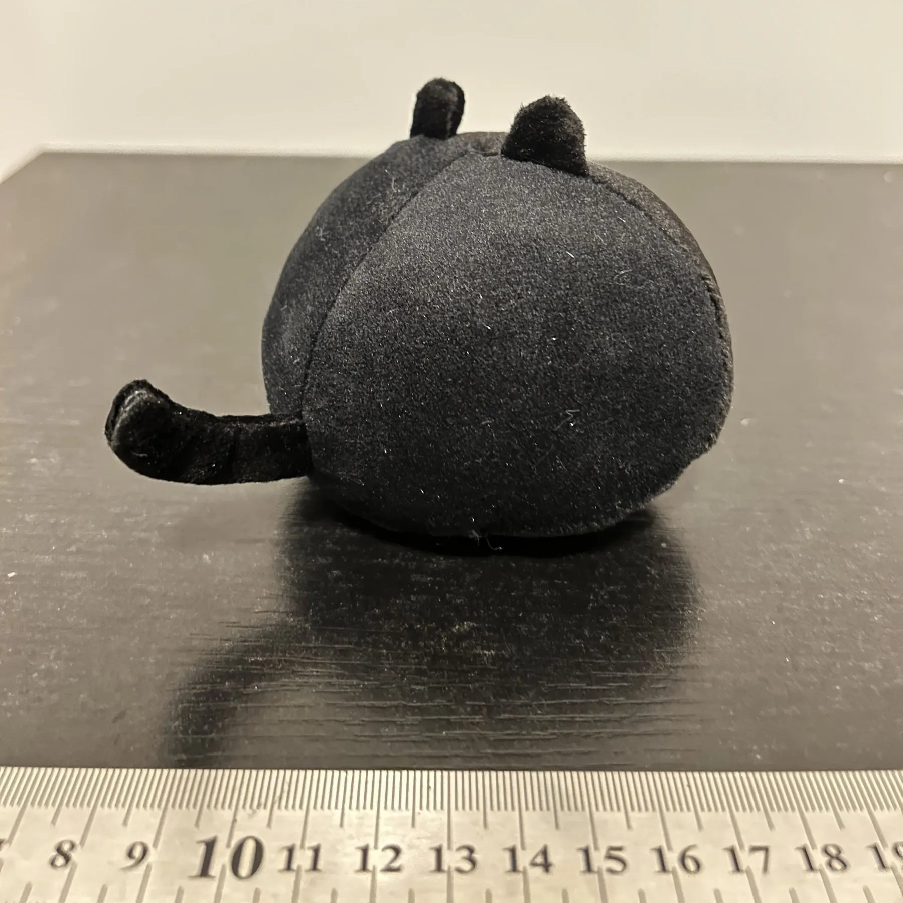 Black fluffy cat plush toy stuffed animal on a sofa, used as a soft cushion.