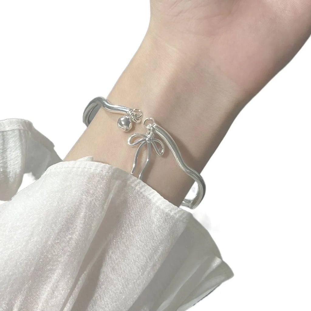 Silver adjustable bracelet with a bow charm and small bell on a zinc alloy band.