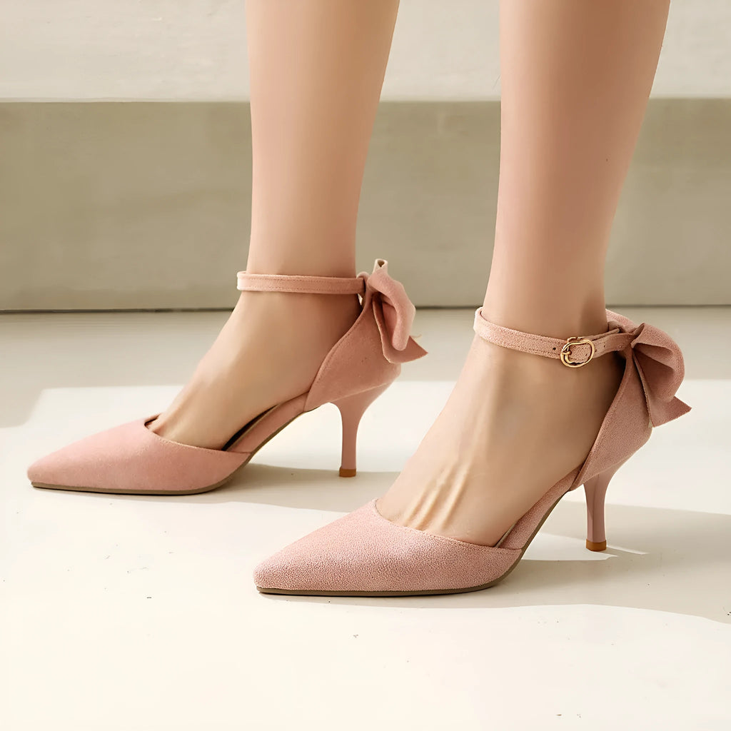 Women's black stiletto high heels with pointed toe, ankle buckle, and a bowknot detail on the suede upper.